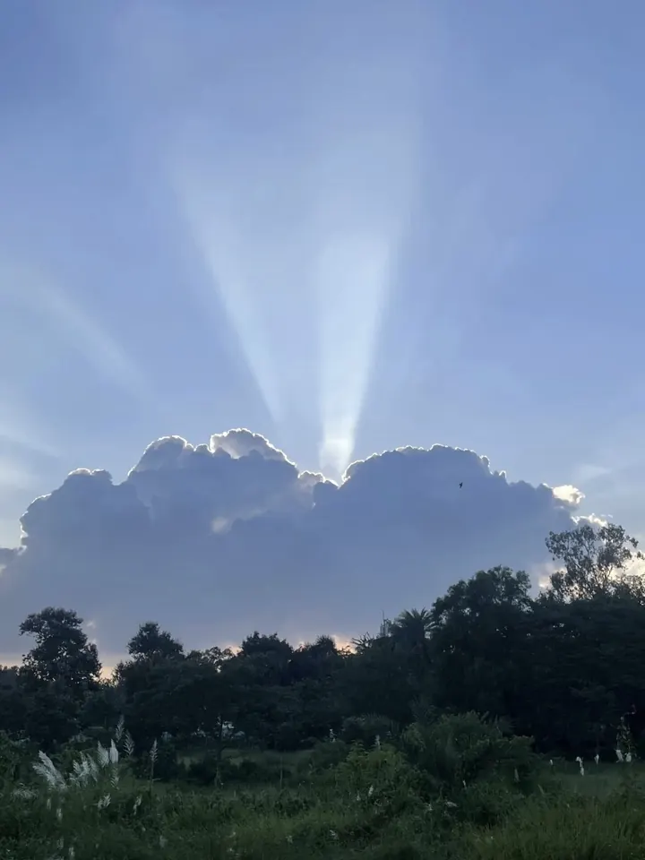 Sun rays breaking through clouds above a green landscape