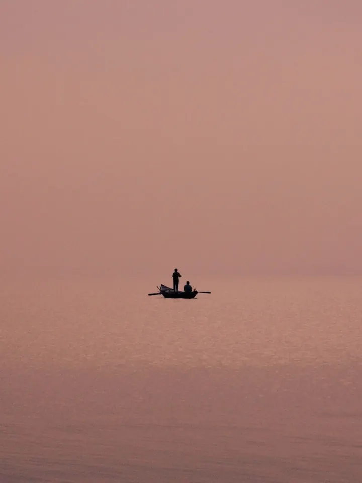 Two people in a small boat on calm pink water