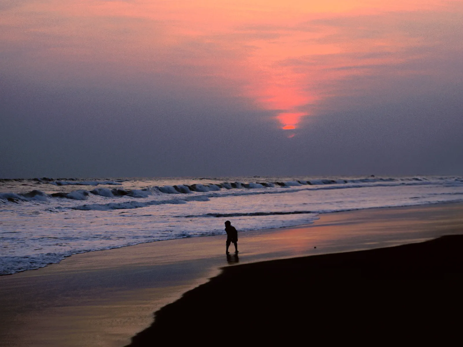 A solitary figure walking along the shoreline at sunset